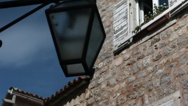 Una linterna frente a la casa. Creativo. Una gran casa de piedra tomada en un ángulo que tiene una ventana en la que crecen pequeñas flores, una linterna y un techo se puede ver — Vídeo de stock