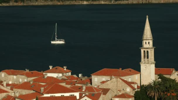 Bela paisagem de um drone. Criativa. Uma pequena vela branca flutua no mar, ao lado do mar há pequenas casas de tijolos e uma torre branca. — Vídeo de Stock