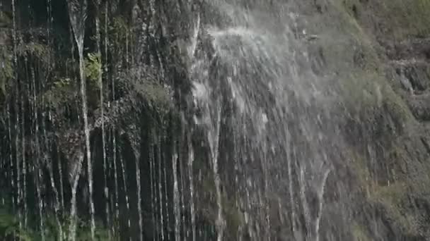 Вид на невеликий водоспад з гори. Творчість. Невеликі краплі води падають на тлі маленьких видимих великих дерев і прожекторів від сонця — стокове відео