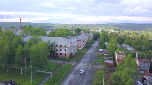 Blick aus einem Hubschrauber. Clip. Ein kleines Dorf mit einer Straße und Autos, umgeben von grüner Sommernatur und hellem Himmel über dem Kopf. — Stockvideo