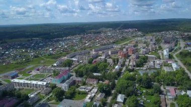 Helikopterden görüntü. Şarjör. İnsanlar için parkları ve evleri olan küçük yeşil bir yaz kasabası, büyük bir orman ve yeşil tarlaları olan tepeler arkadan görülüyor