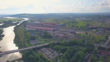 Helikopterden görüntü. Şarjör. Nehiri olan küçük bir kasaba, arabaları, küçük evleri ve arka planda dağları olan bir köprü..