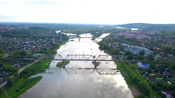 Krásný výhled z helikoptéry. Klip. Pohled na řeku, přes kterou jsou mosty, vedle řeky jsou obytné budovy, zelené hory a jasně bílá obloha — Stock video