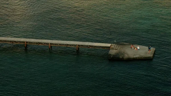 Un largo puente sobre el mar. La vista desde el dron. Creativo. Un mar azul ondulado con un puente largo sobre él donde la gente se relaja tomar fotos y nadar — Foto de Stock