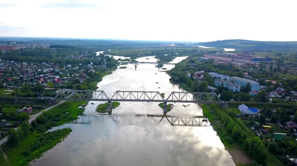 Krásný výhled z helikoptéry. Klip. Pohled na řeku, přes kterou jsou mosty, vedle řeky jsou obytné budovy, zelené hory a jasně bílá obloha — Stock fotografie