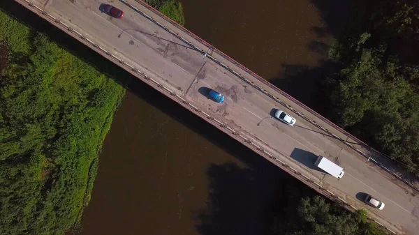 Uma pequena ponte sobre o rio. Clipe. A vista do drone. Um rio estreito através do qual há uma ponte alta em que os carros dirigem ao lado de grama verde e árvores . — Fotografia de Stock