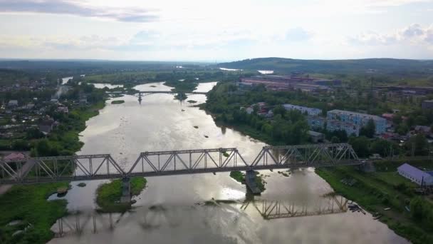 Krásný výhled z helikoptéry. Klip. Pohled na řeku, přes kterou jsou mosty, vedle řeky jsou obytné budovy, zelené hory a jasně bílá obloha 