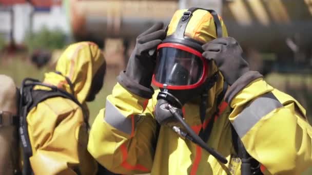 Człowiek dopasowuje maskę gazową. Klip. Pracownik noszący maskę gazową i żółty garnitur to pracownik na świeżym powietrzu, który idzie od tyłu. — Wideo stockowe