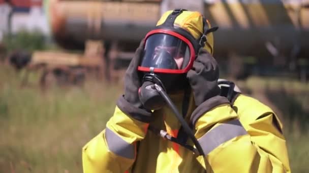 Człowiek dopasowuje maskę gazową. Klip. Pracownik noszący maskę gazową i żółty garnitur to pracownik na świeżym powietrzu, który idzie od tyłu. — Wideo stockowe
