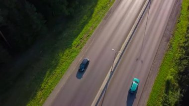 Forest Highway boyunca giden siyah arabanın üst görüntüsü. Şarjör. Yeşil ormanın arka planında otoyol boyunca giden bir araba. Güneşli bir yaz gününde orman yolunda arabayla seyahat etmek.