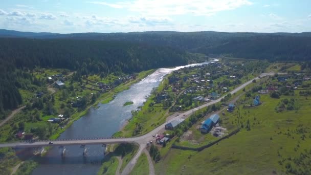 Vista de pájaro. Clip. Un hermoso gran bosque junto a pequeñas casas y una zona residencial y un gran río largo y un cielo brillante desde arriba. — Vídeos de Stock