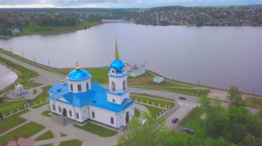 Bir yaz günü şehrin pitoresk alandaki hava manzarası. Şarjör. Mavi çatılı bir kilise, bir gölet ve uzak mesafedeki şehirlerde arka planda orman dağları olan evler..
