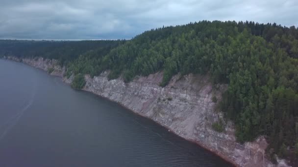 Flygfoto över den branta klippan ovanför den lugna flodytan. Klipp. Grön tallskog på kullar och vattenyta. — Stockvideo