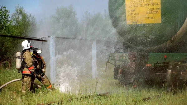 Munkafolyamat. Csípés. Egy tűzoltó egyenruhában és sisakban habot használ. . — Stock Fotó