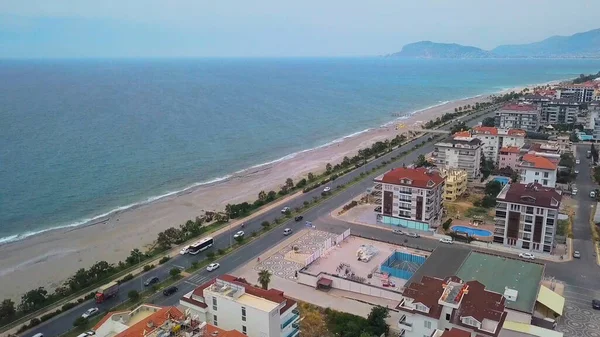 Utsikten från drönaren. Klipp. Den vidsträckta havet med stranden, intill vägen med bilar och även en liten bit av staden med stora hus. — Stockfoto
