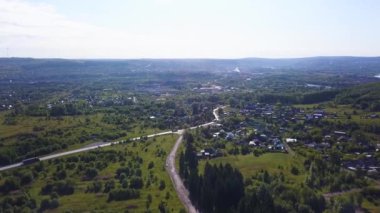Helikopterden yaz manzarası. Şarjör. Otoyolu olan küçük bir kasaba, konut binaları, konut binaları, parklar ve ormanlar ve etrafındaki ağaçlar güneşli gökyüzünde.
