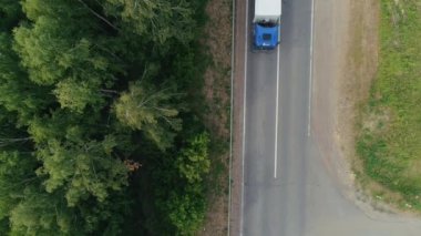 Helikopterden görüntü. Sahneler. Mavi önlü bir kargo kamyonu ve taşımacılık karavanı olan bir aracın bulunduğu dar bir yol, yakınlarda çimenli bir orman ve yol var. .