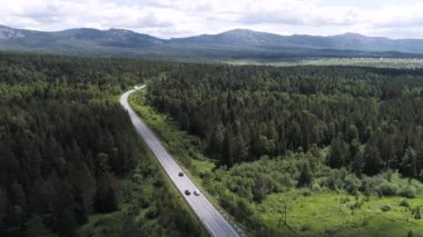 İnsansız hava aracından güzel bir yaz doğası. Sahneler. Güzel dağları olan güzel bir manzara, yeşil bir orman, arabaların parlak bir gökyüzü ve çimlerle sürdüğü bir yol..