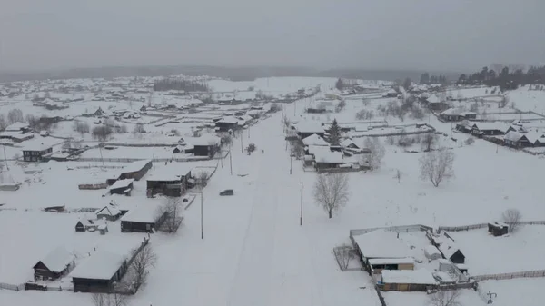 Vista a volo d'uccello innevata. Clip. Un villaggio bianco nella neve con piccole case in legno e accanto ad essa una grande foresta con alberi alti — Foto Stock