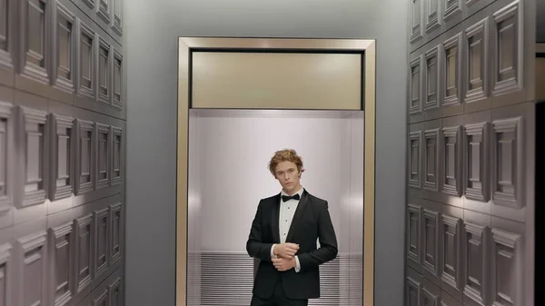 Hermoso novio con estilo en el interior del hotel posando frente a la cámara. Acción. Hombre en traje negro y camisa blanca de pie junto a la pared en el extremo del pasillo. —  Fotos de Stock