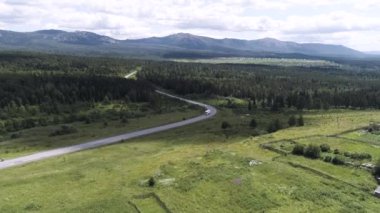 İnsansız hava aracından güzel bir yaz doğası. Sahneler. Güzel dağları olan güzel bir manzara, yeşil bir orman, arabaların parlak bir gökyüzü ve çimlerle sürdüğü bir yol..