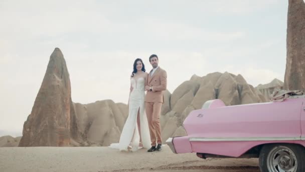 Gyönyörű fiatal pár fotózás közben egy hegytetőn Cappadociában. Felvétel. Romantikus szerelem a férfi és a nő pár közelében kabrió rózsaszín autó. — Stock videók