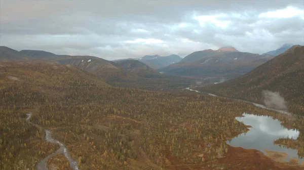 Vista aérea da floresta colorida de outono, lagos e pântanos sob o céu nublado. Clipe. Terreno montanhoso, paisagem natural selvagem, Taiga, Rússia. — Fotografia de Stock