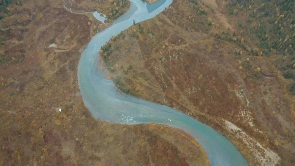 Naturaleza desde la altura de un dron. Clip. El río azul claro y sinuoso junto al bosque gris fluye a través de las cadenas montañosas. —  Fotos de Stock