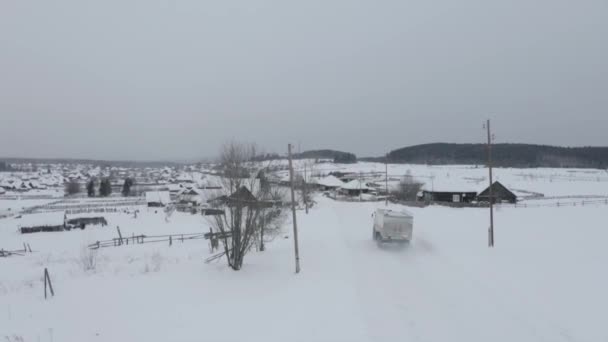 Κάτοψη του μικρού χωριού το χειμώνα. Κλιπ. Φορτηγό οδηγεί μέσα από μικρό παλιό χωριό το χειμώνα. Χειμερινό τοπίο με παλιό σπάνιο χωριό σε συννεφιασμένη ημέρα — Αρχείο Βίντεο