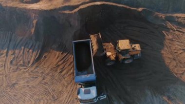 Taş ocağında çöp kamyonu olan kazıcının üst görüntüsü. Sahne. Kazıcı, taş ocağındaki çöp kamyonunu toprakla dolduruyor. İnşaat için geniş bir alanı yağmalamak