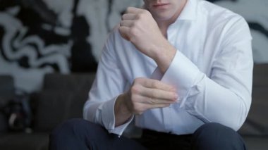 Adam giyiniyor ve düğmelerini beyaz gömleğinin kollarına takıyor. Başla. Erkek kollarını kapat, adam oturur ve düğmelerini iliklemeye çalışır..