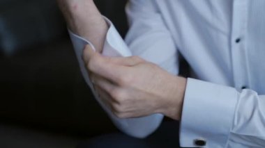 Adam giyiniyor ve düğmelerini beyaz gömleğinin kollarına takıyor. Başla. Erkek kollarını kapat, adam oturur ve düğmelerini iliklemeye çalışır..