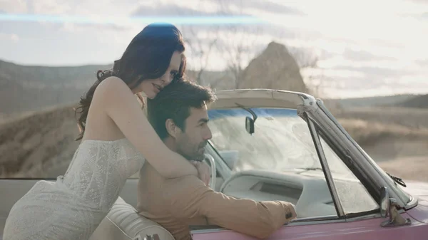 Uma bela sessão de fotos interessante dos recém-casados. Acção. A noiva de aparência bonita em um vestido longo branco bonito estreito com seu noivo bonito em um terno marrom são fotografados posando ao lado de — Fotografia de Stock