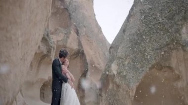 Cappadocia Dağları 'nda romantik kar yağışı altında genç ve güzel bir çift. Başla. Gelin ve damat, kar tanelerinin altında sıradışı kaya oluşumlarıyla çevrili vadide birlikte duruyorlar..