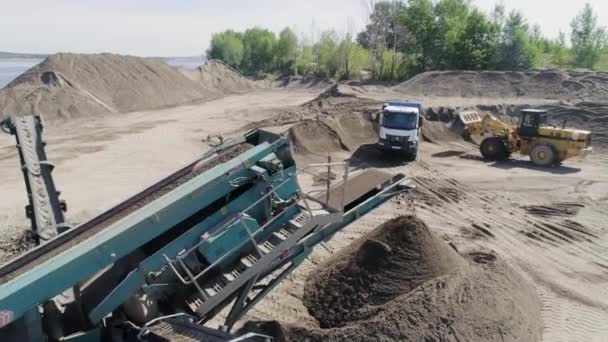 Het bouwproces. Plaats delict. Vrachtwagens vervoeren materialen voor de bouw in een leeg gebied waarachter zich een rivier, bossen, blauwe lucht — Stockvideo