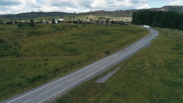 Road view from the drone .Scene. A bright summer road on which a truck is driving and fields with a green forest and beautiful nature against a blue sky and a village behind. — Stock Video