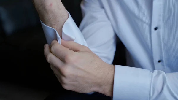 El hombre se viste y hace sus botones en las mangas de su camisa blanca. Acción. Acercamiento de los brazos masculinos, hombre sentado y tratando de abotonar. —  Fotos de Stock