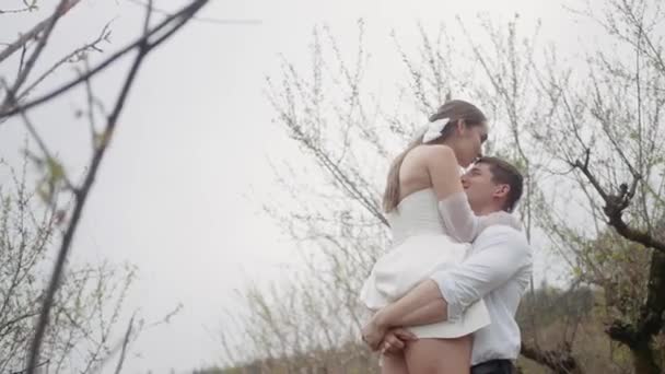 Beautiful couple embraces in spring garden. Action. Couple of newlyweds enjoy first leaves and flowers in garden in spring. Couple embraces in blooming garden in early spring — Vídeo de Stock