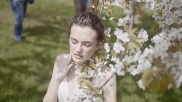 Beautiful young woman with cherry blossom branches. Action. Poetic image of beautiful woman with blooming apple tree. Beautiful woman in white dress with flowering tree — Stock Video