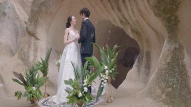 Rock arka planında güzel yeni evliler. Başla. Kar yağarken mağaranın arka planında yeni evlilere sarılmak. Kar yağarken kayalıklarda düğün töreni