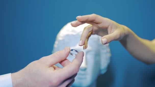 Close-up husband puts ring on brides finger. Action. Marriage combination of newlyweds with rings on isolated background. Groom puts ring on bride on background of plaster bust — Stock Video