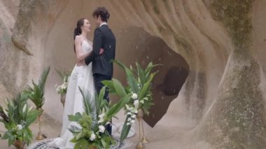 Rock arka planında güzel yeni evliler. Başla. Kar yağarken mağaranın arka planında yeni evlilere sarılmak. Kar yağarken kayalıklarda düğün töreni