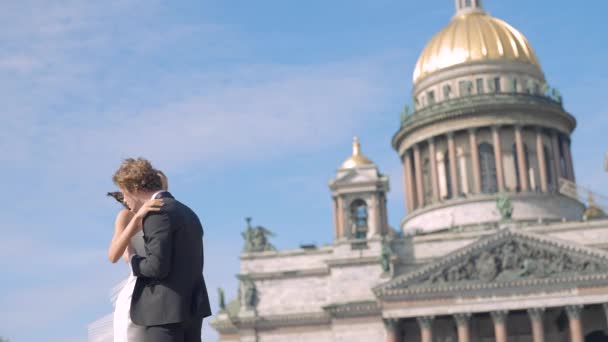 Photosession of a beautiful elegant wedding couple on the background of St. Isaac s Cathedral. Action. Loving Bride and groom embracing at the historical center of Saint Peterburg, Russia. — стокове відео