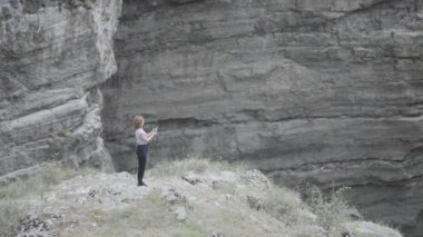 Kadın telefonda dağ gibi sabit bir resimle fotoğraf çekiyor. Başla. Dağlarda kayaların arasında güzel bir kadın telefonla fotoğraf çekiyor. Kadın profesyonel olarak kaya manzaraları ve şelaleler vuruyor.