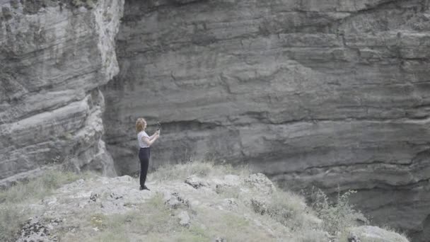 Woman takes pictures on phone with steadicam of mountain. Action. Beautiful woman in the mountains among rocks takes pictures on phone. Woman professionally shoots rock landscapes and waterfalls on — Stockvideo