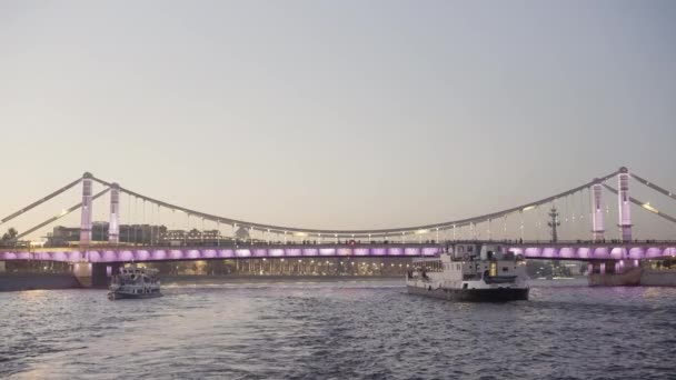 Bellissimo fiume increspato attraversato dal ponte decorato da luci. Azione. Yacht turistici attraversando ampio fiume sul sfondo cielo tramonto. — Video Stock