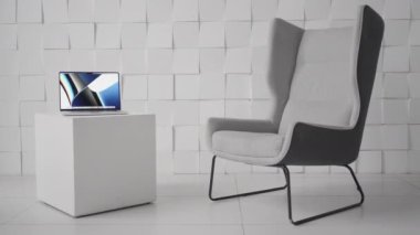 Modern bir ofiste kübik şekilli bir sehpada dizüstü bilgisayar. Başla. Odanın minimalist tasarımı, rahat bir sandalye ve küçük bir masa üzerinde bilgisayar..