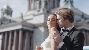 Damadın portresi, sırtından sarılan beyaz elbiseli genç gelinin portresi. Başla. Saint Petersburg, Rusya 'daki St. Isaac Katedrali önünde düğün fotoğrafı çekilmesi.