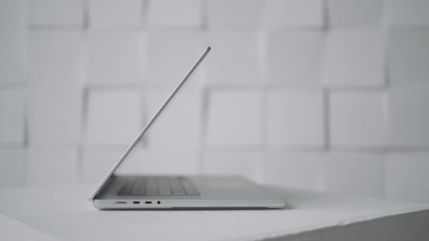 Widok z boku nowego nowoczesnego białego laptopa leżącego na powierzchni stołu pod ścianą. Akcja. Praca w domu, koncepcja wolnego strzelca. — Wideo stockowe