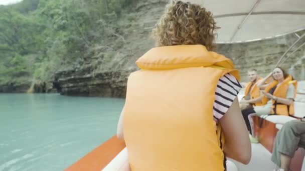 관광객들은 푸른 산을 따라 요트를 타고 여행하고 배를 탑니다. 행동. 강의 청록색 물 과 구명 자켓을 입은 사람들. — 비디오